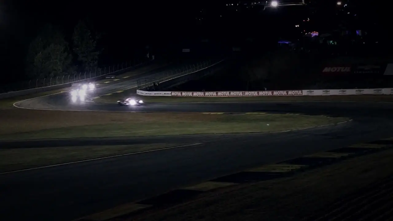 Phares qui surgissent d'un virage sur un circuit, de nuit